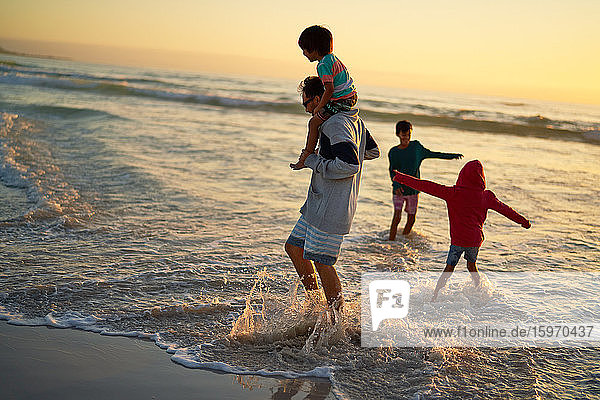 Familie planscht und spielt in der Meeresbrandung bei Sonnenuntergang