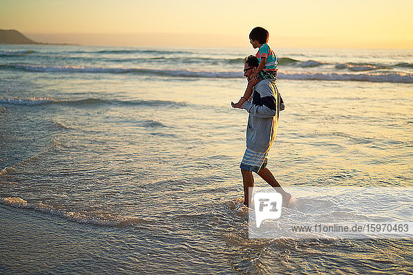 Father carrying son on shoulders in ocean surf at sunset