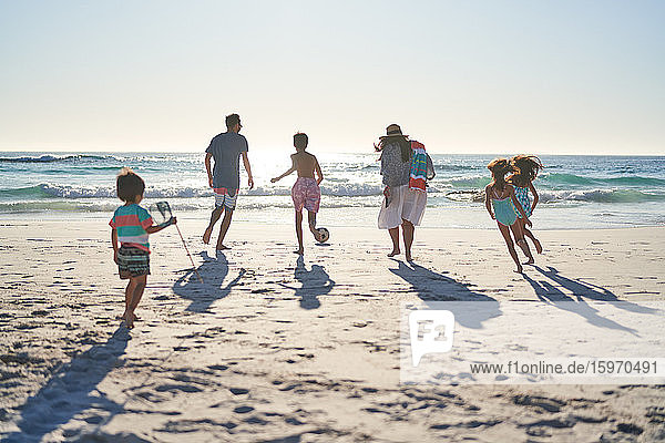 Family running and playing soccer on sunny ocean beach