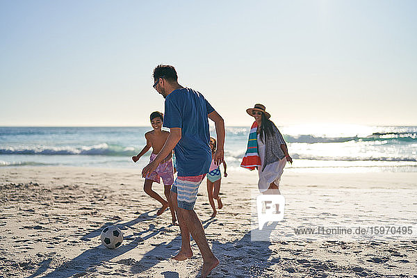 Family playing soccer on sunny ocean beach