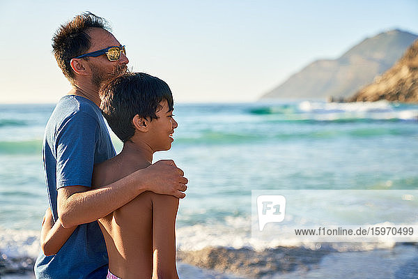 Affectionate father and son hugging on sunny ocean beach