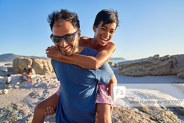 Glücklicher Vater nimmt Sohn huckepack am sonnigen Strand