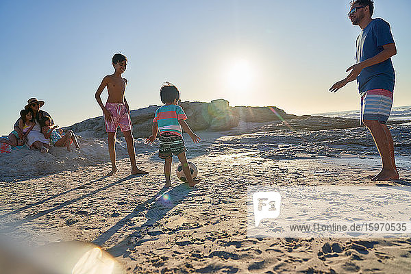 Familie spielt Fussball am sonnigen Strand