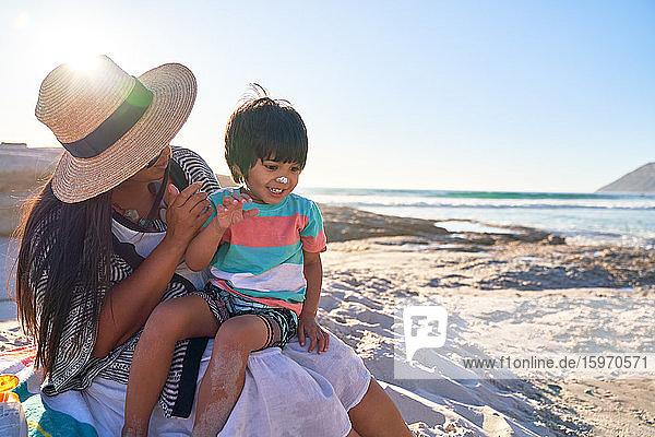 Mutter trägt Sonnencreme auf die Nase ihres süßen Sohnes am sonnigen Strand auf