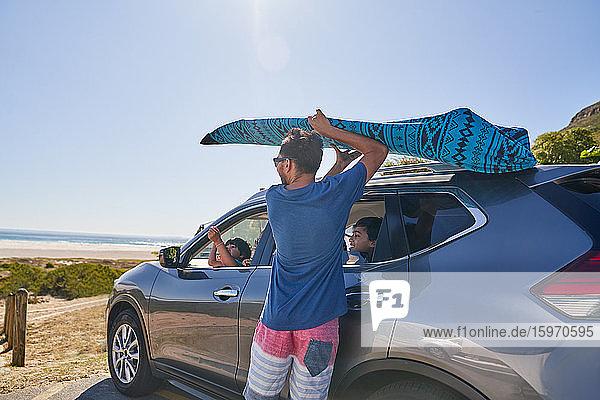 Man removing surfboard from top of car in beach parking lot