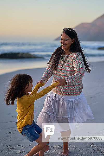 Verspielte Mutter und Tochter tanzen am Strand