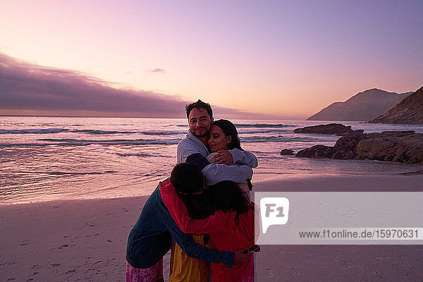 Porträt einer glücklichen Familie  die sich am Strand bei Sonnenuntergang am Meer umarmt  Kapstadt