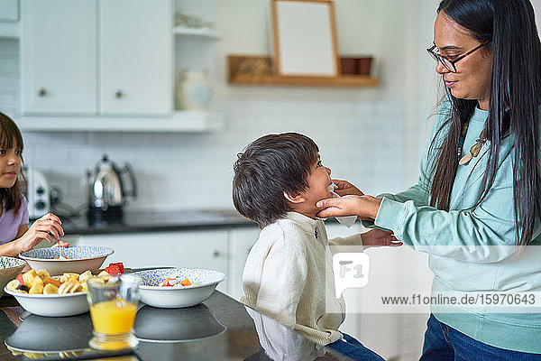 Mutter wischt dem Sohn das Gesicht ab  der in der Küche Obst isst