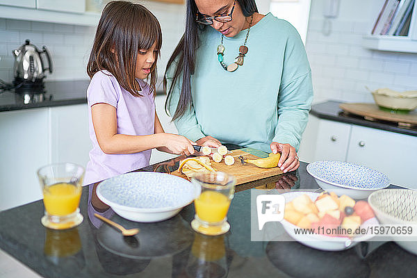 Mutter hilft Tochter beim Bananenschneiden in der Küche