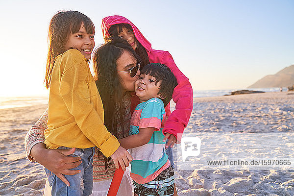 Zärtliche Mutter küsst Kinder am sonnigen Strand