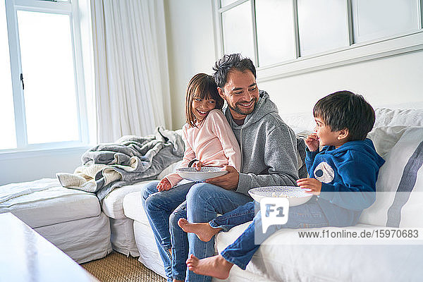 Glücklicher Vater und Kinder essen Popcorn auf dem Wohnzimmersofa