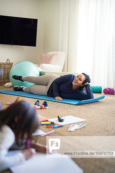 Smiling mother exercising while daughter draws in living room