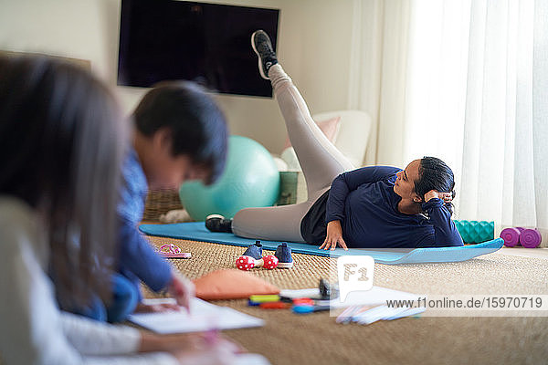 Mother exercising in living room with kids coloring nearby