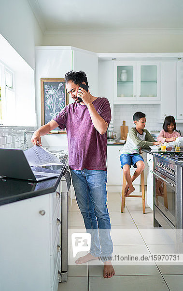 Father working at laptop in kitchen with kids eating