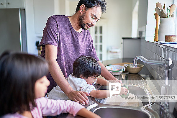 Vater und Kinder beim Abwasch an der Küchenspüle