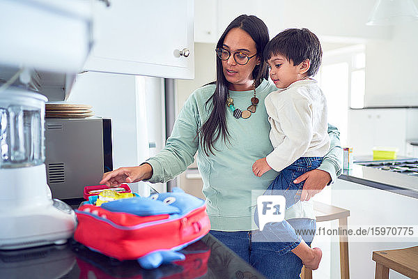 Mother holding son and preparing school lunch in kitchen