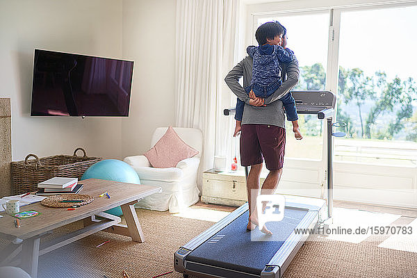 Father piggybacking son on treadmill in sunny living room