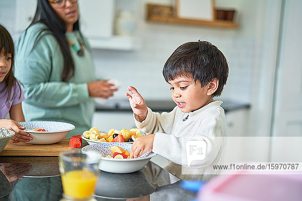 Cute boy eating fresh fruit in kitchen
