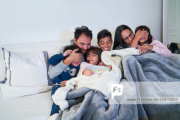Glückliche Familie schaut Gruselfilm auf Wohnzimmersofa