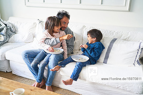 Vater und Kinder essen Popcorn auf dem Wohnzimmersofa