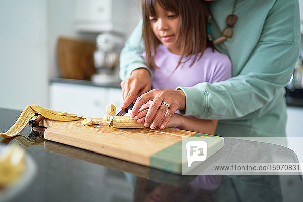 Mother helping daughter cut banana in kitchen
