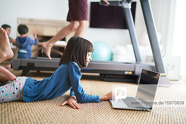 Mädchen benutzt Laptop auf dem Boden neben dem Vater auf dem Laufband