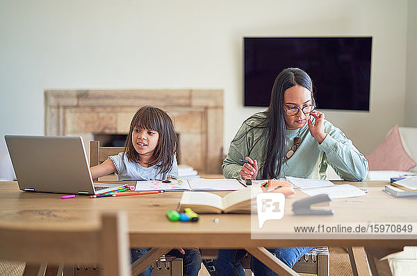 Mother paying bills next to daughter homeschooling at table