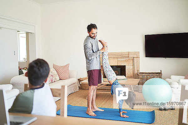 Father helping daughter to handstand on yoga mat in living room