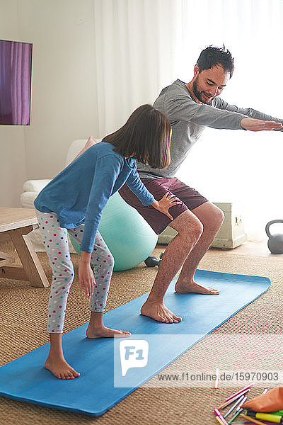 Father and daughter exercising on mat in living room