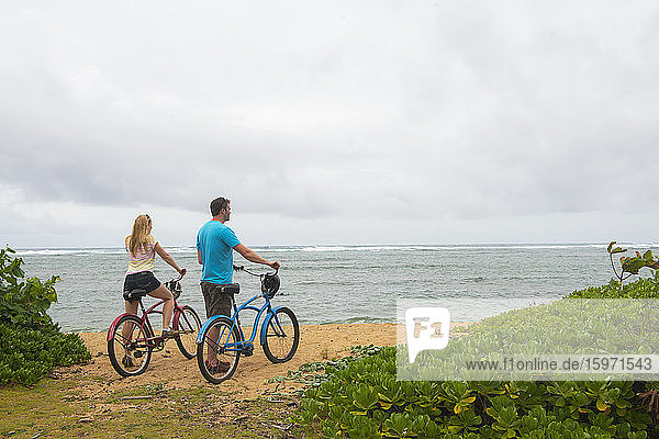 Couple with bicycles looking out at the ocean on Kauai near Kapaa  Hawaii  United States of America  North America