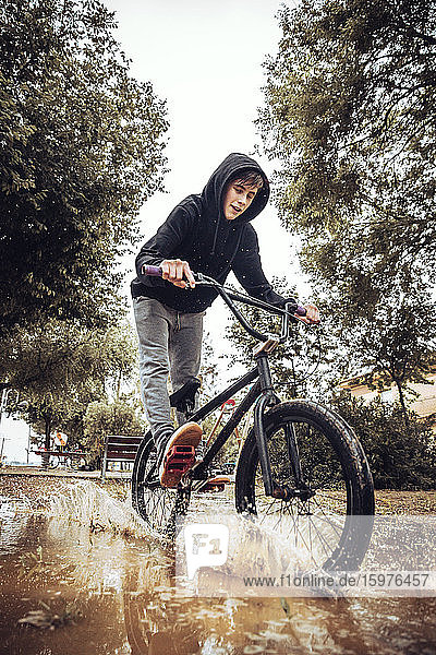 Jugendlicher  der beim Radfahren in der Regenzeit Wasser in eine Pfütze spritzt