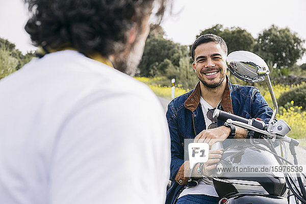 Lächelnder Mann im Gespräch mit einem Motorradfahrer auf einem Motorrad sitzend