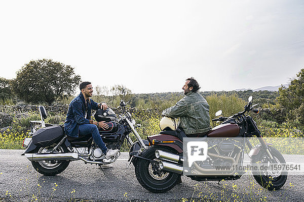 Männliche Biker  die sich auf Motorrädern sitzend gegen den Himmel unterhalten