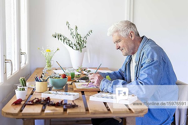 Älterer Mann malt auf dem Tisch zu Hause
