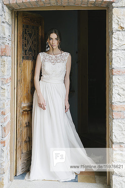 Young woman in wedding dress walking through door