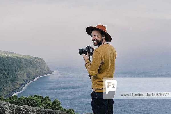 Lächelnder Mann mit einer Kamera an der Küste der Insel Sao Miguel  Azoren  Portugal