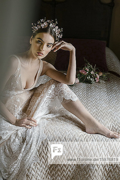 Junge Frau im Hochzeitskleid sitzt auf dem Bett und schaut zur Seite