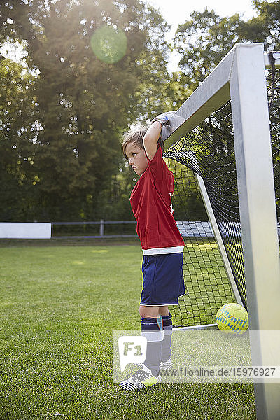 Junge in Fußballtrikot hält Torpfosten am Spielfeld