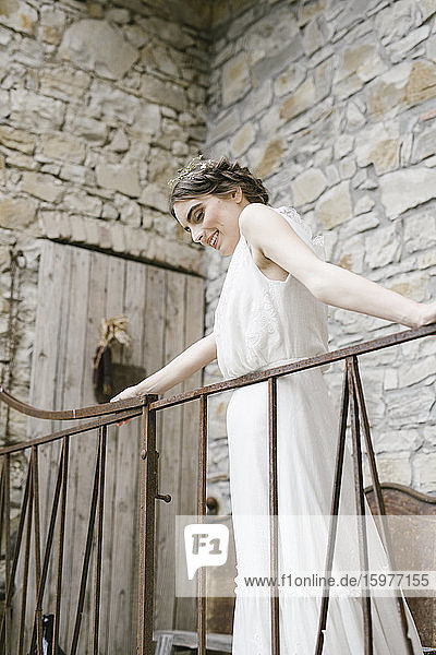 Junge lächelnde Frau in elegantem Hochzeitskleid am Geländer