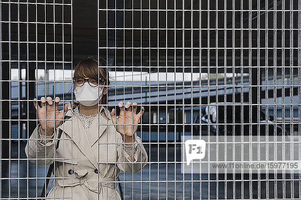 Frau mit Gesichtsmaske steht hinter einem Gitter in einem Parkhaus