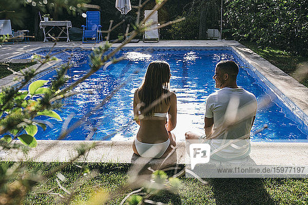Rückansicht eines jungen Paares  das am Pool sitzt und sich unterhält