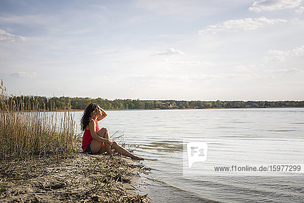 Junge Frau sitzt am Seeufer und genießt das Sonnenlicht