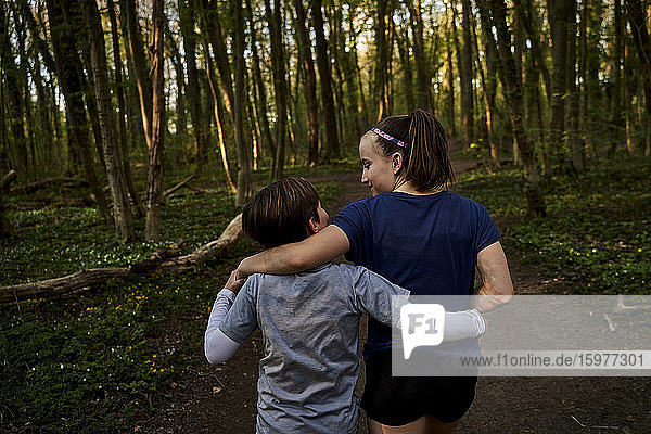 Rear view of sibling walking with arm around in forest