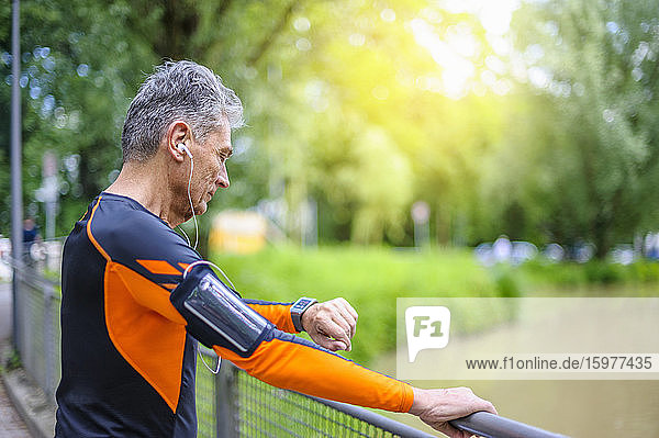 Side view of active senior man looking at smart watch by railing at park