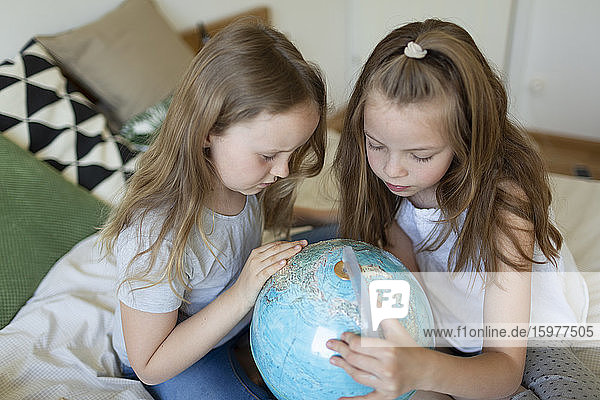Zwei Schwestern sitzen zusammen auf einem Bett und betrachten einen Globus