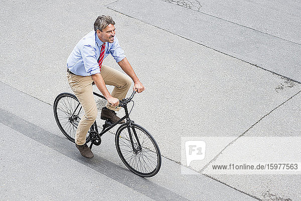 Smiling businessman riding bicycle on street in city