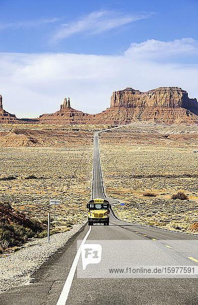 School bus drives on desert road at Monument Valley Tribal Park against sky  Utah  USA