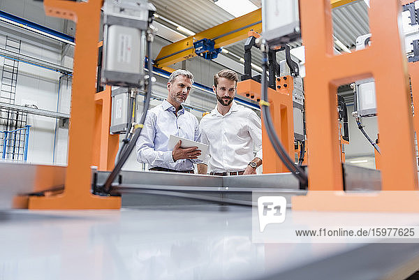 Zwei Männer mit einem Tablet betrachten eine Maschine in einer Fabrikhalle