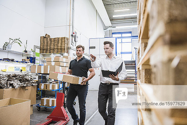Two men with parcel and clipboard in storehouse of a factory