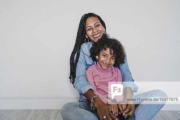 Porträt einer glücklichen Mutter und ihrer kleinen Tochter  die zusammen auf dem Boden sitzen